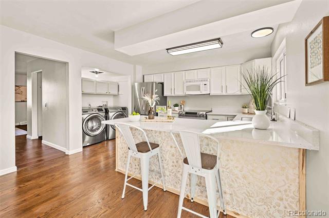 Bright kitchen with white cabinets, a breakfast bar, and a laundry area at left.