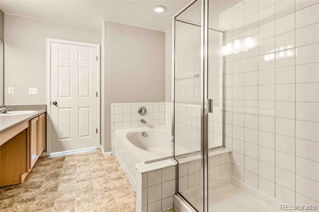 Bathroom with a glass-enclosed tiled shower, built-in tub, and wood vanity.