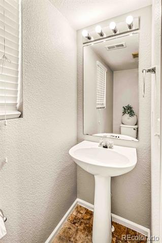 Small bathroom with a white pedestal sink, large mirror, vanity lights, and brown patterned tile floor.