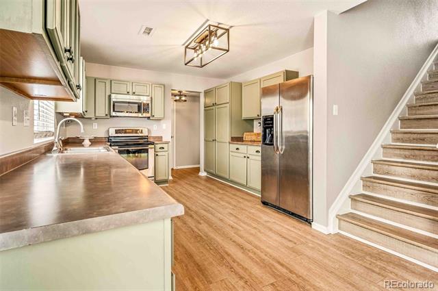 Kitchen with pale green cabinets, stainless steel appliances, brown countertops, and an adjacent staircase.