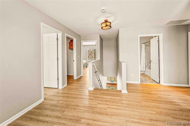 Vacant upper-level landing with light wood floors, gray walls, and an open stairwell.