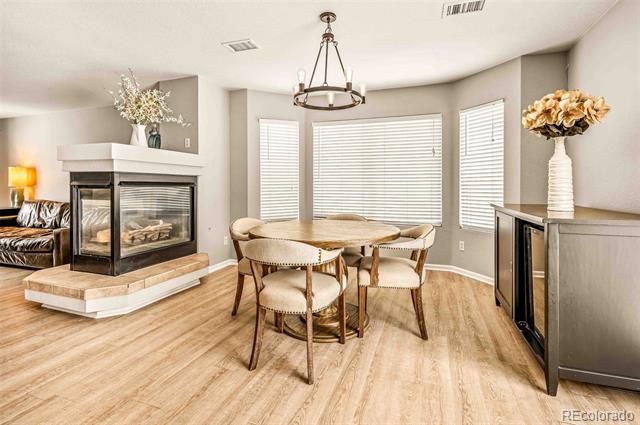 Dining area with a round table beside a glass-front fireplace and large windows.