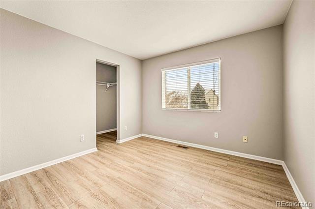 Empty bedroom with wood-look flooring, a window with blinds, and an open closet.