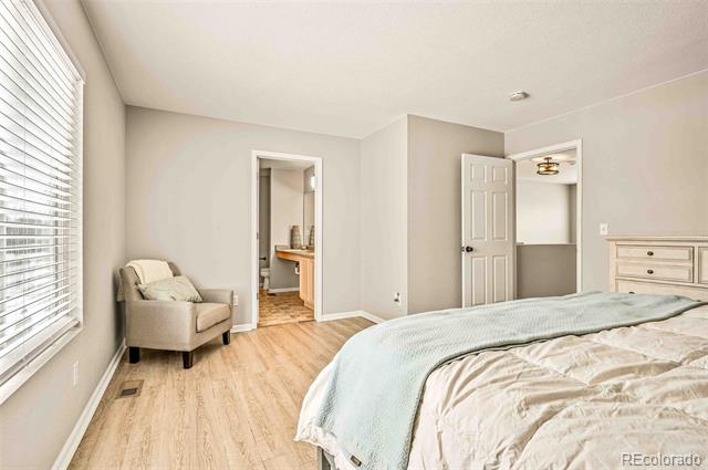 Bedroom with pale bedding, light wood floors, and an armchair beside a window.