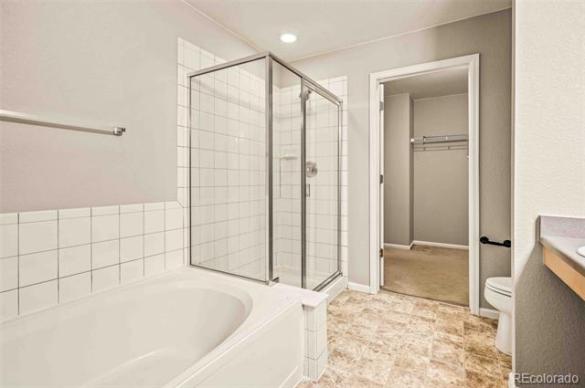 Bathroom with a soaking tub, glass-enclosed shower, and doorway to a carpeted closet.