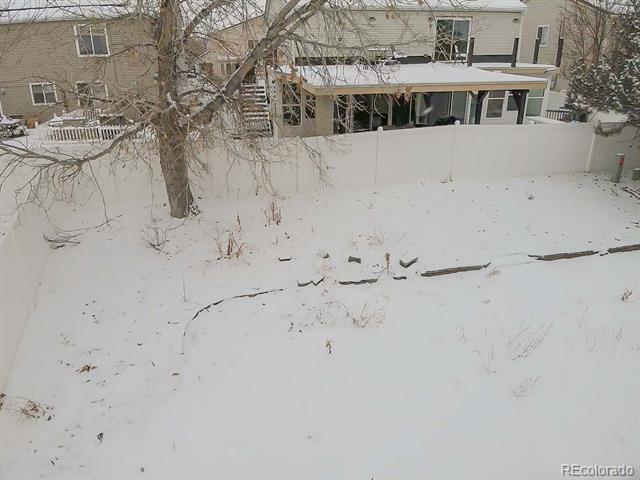 Snow-covered fenced backyard with a large leafless tree and covered patio.