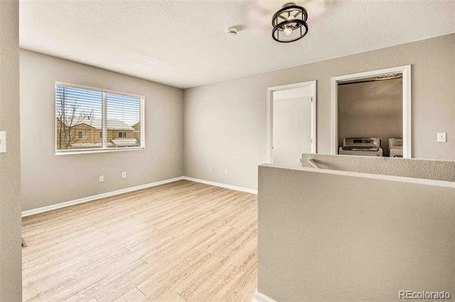 Empty dining area with light wood flooring, a wide window, and a half wall adjoining the kitchen.
