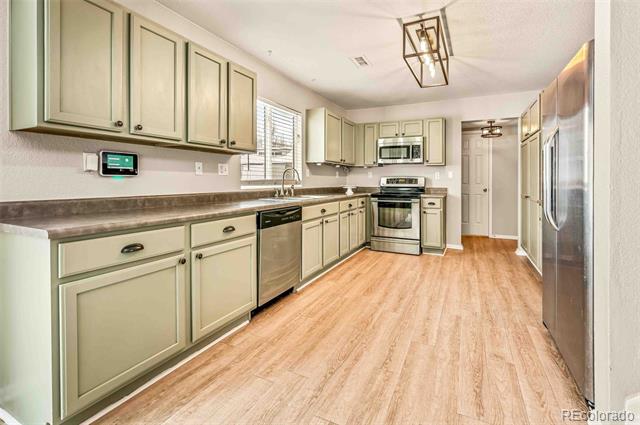 Kitchen with pale green cabinets, stainless steel appliances, and light wood flooring.