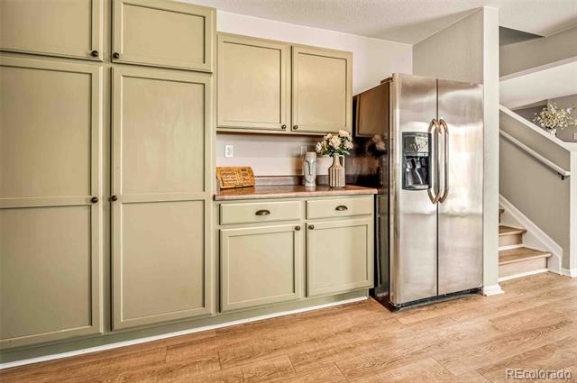 Kitchen with sage-green cabinetry, stainless-steel refrigerator, dark countertop, and adjacent staircase.