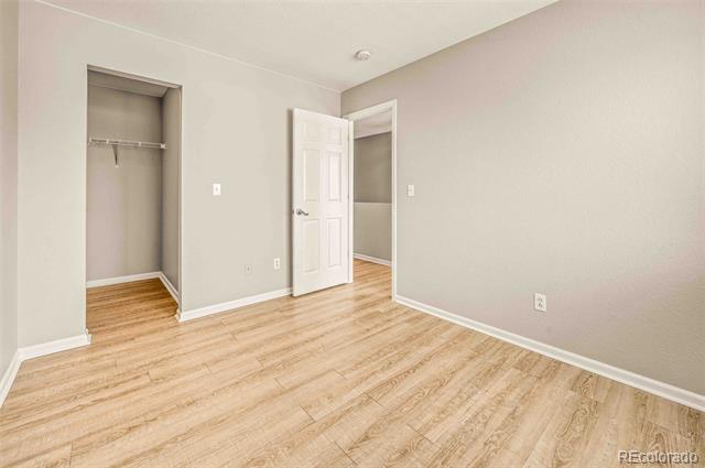 Vacant bedroom with light wood-look flooring, an open closet, and a door to another room.