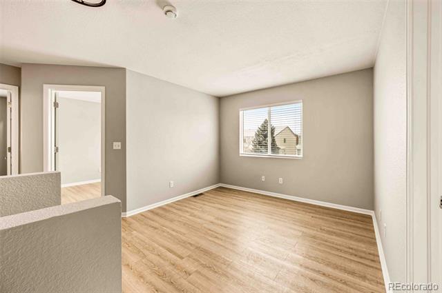 Empty room with light wood-look flooring, gray walls, and a window with blinds.