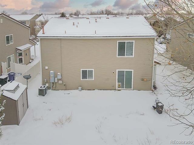Rear of a beige-sided home with a snow-covered roof and backyard.