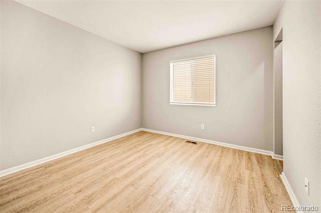 Empty room with light wood flooring, pale walls, and a window with blinds.