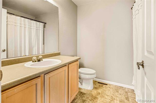 Bathroom with a wood vanity and tiled floor, toilet, and shower curtain reflected in the mirror.