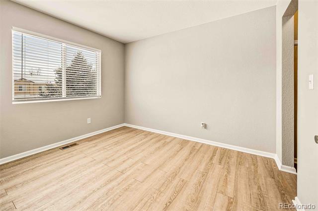 Empty room with light wood-look flooring and a wide window with blinds.