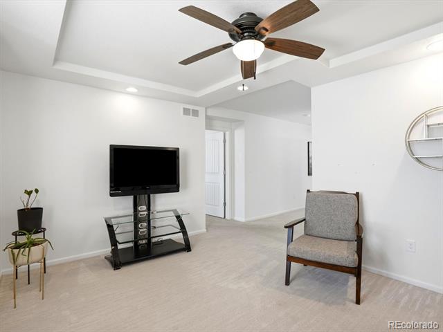 Living room with a dark wood ceiling fan, glass TV stand, potted plant, and gray upholstered chair.