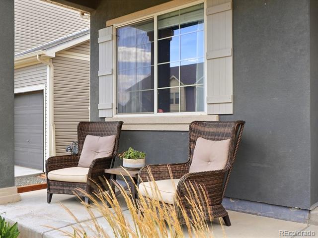 Covered home porch with two wicker chairs, pale cushions, and a shuttered window.