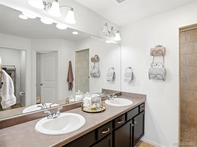 Bathroom with a double-sink vanity, dark cabinetry, large mirror, and tiled shower.