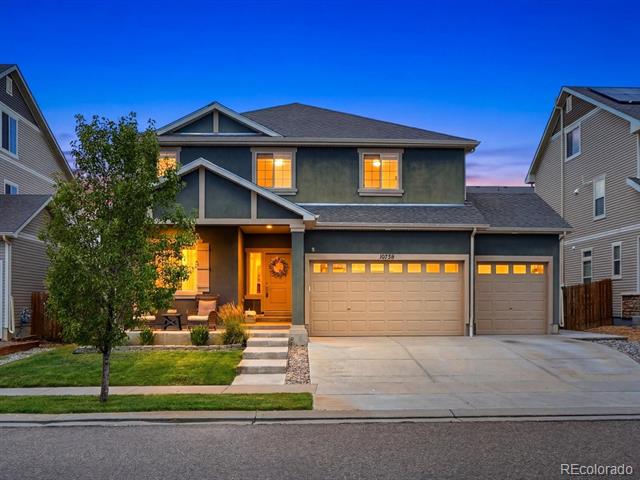 Two-story gray home with a three-car garage and warmly lit windows at dusk.