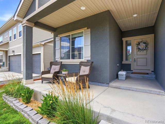 Home exterior with a covered porch, two cushioned chairs, and landscaped plants along the walkway.