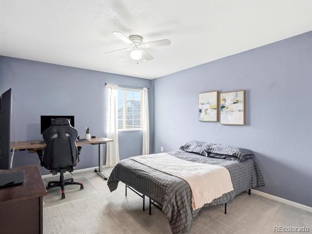 Bedroom with a gray bed and gaming desk beside a bright window.