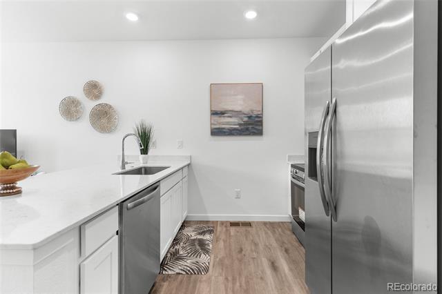 Modern white kitchen with stainless steel appliances, a patterned runner, and wood-look flooring.