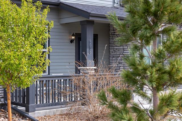 Home’s covered front porch with gray siding, dark railing, and leafy trees in the foreground.