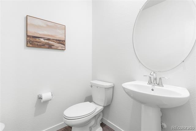 Half bathroom with a white pedestal sink, round mirror, toilet, and landscape artwork.