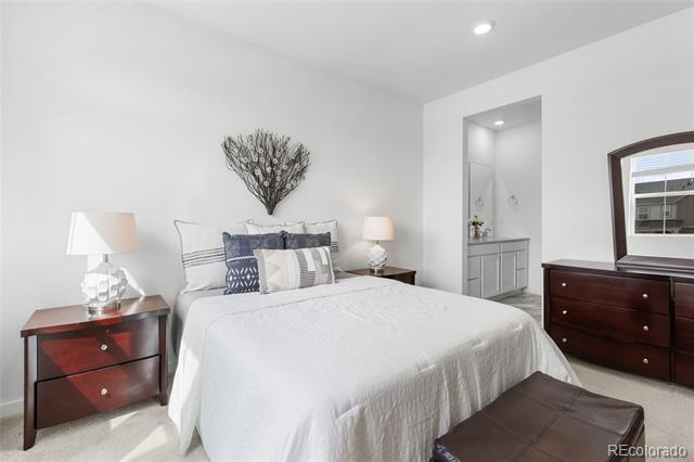 Staged bedroom with white bedding, dark wood furniture, and an en-suite bathroom doorway.