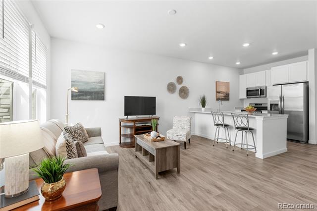Open-plan living room and kitchen with a gray sectional, white cabinets, stainless steel appliances, and breakfast island.