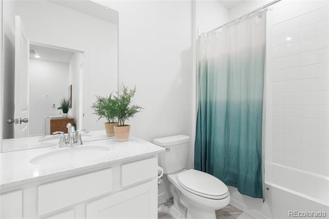 Bright bathroom with white vanity, toilet, and teal ombré shower curtain.