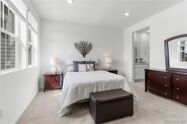Furnished bedroom with a white bed, dark wood furniture, leather ottoman, and large windows.