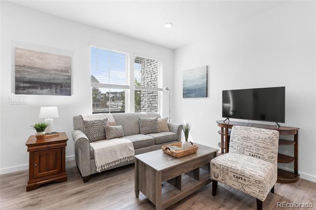 Living room with a gray sofa, patterned armchair, and television beside large windows.