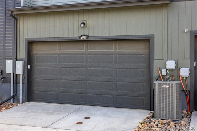 Gray paneled garage door with a concrete driveway and utility equipment beside it.