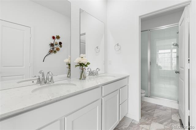Bright bathroom with a white double-sink vanity and adjoining glass-enclosed shower.