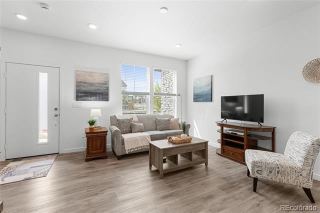 Staged living room with gray sofa, wood coffee table, television, and large windows.