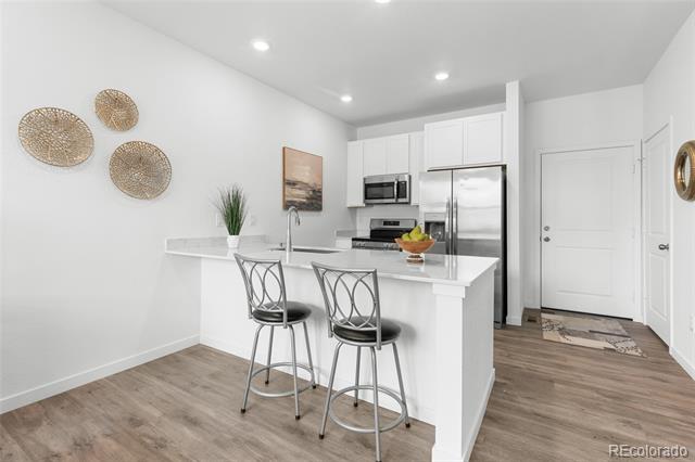 Bright kitchen with a white island, stainless steel appliances, and two metal bar stools.