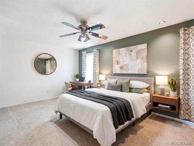 Staged bedroom with a large bed, ceiling fan, round mirror, and desk beside the window.