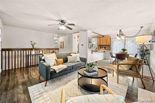 Open-plan living and dining area with a gray sofa, tan armchairs, and kitchen beyond.