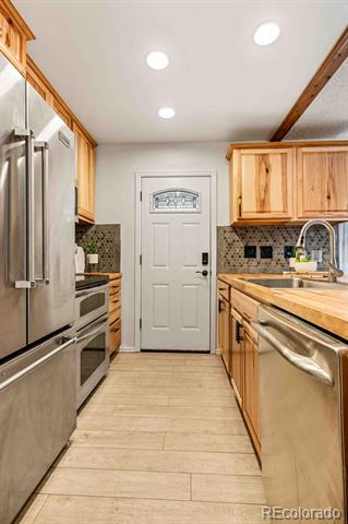 Galley kitchen with light wood cabinets, stainless steel appliances, and a white door at the far end.