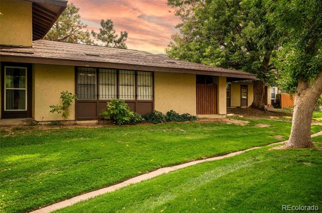 Single-story tan stucco home with a long roof, dark-trimmed windows, and a green front lawn.