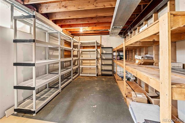 Unfinished basement storage room with metal and wooden shelving and exposed ceiling joists.