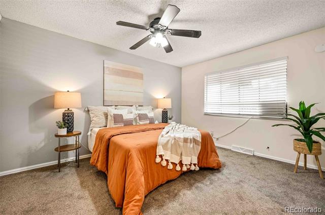 Bedroom with an orange bedspread, matching bedside lamps, and a potted plant by the window.