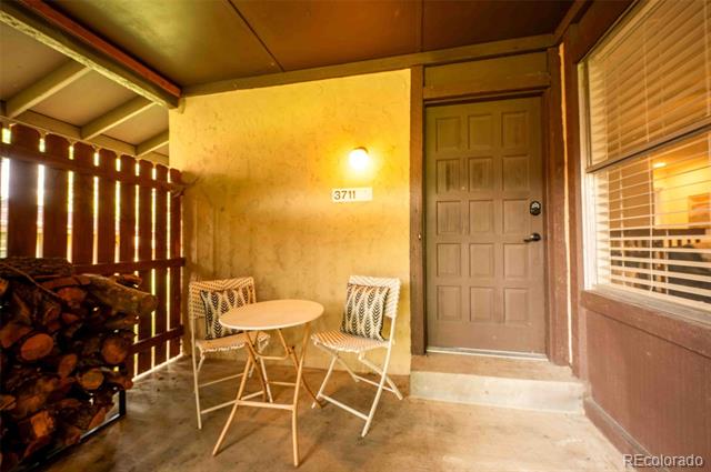 Covered entry porch with a brown paneled door, two chairs, and stacked firewood.