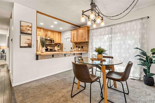 Dining area with a round glass table, brown chairs, and an adjoining light-wood kitchen.