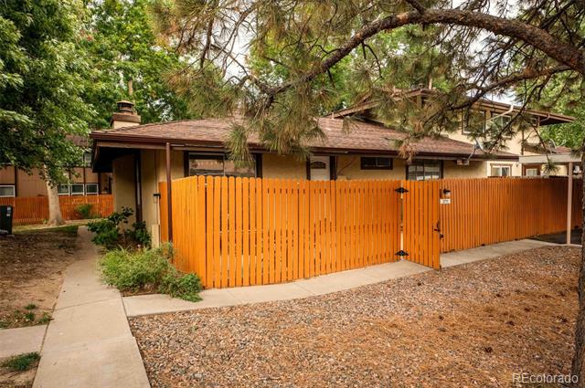 Single-story home behind an orange wooden privacy fence, shaded by mature trees.