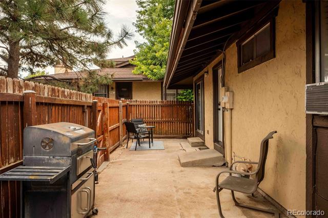Fenced concrete patio beside the house, with a barbecue grill and outdoor seating.