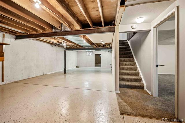 Unfinished basement with exposed ceiling joists, a concrete floor, and carpeted stairs.