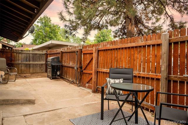 Concrete patio with a glass-top table, chairs, outdoor grill, and tall pine tree.