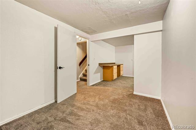 Basement room with beige carpet, a small wooden counter, and stairs through an open doorway.